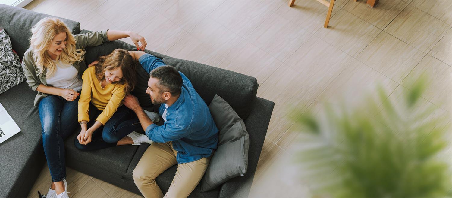 A mother, father, and daughter sitting on a gray couch