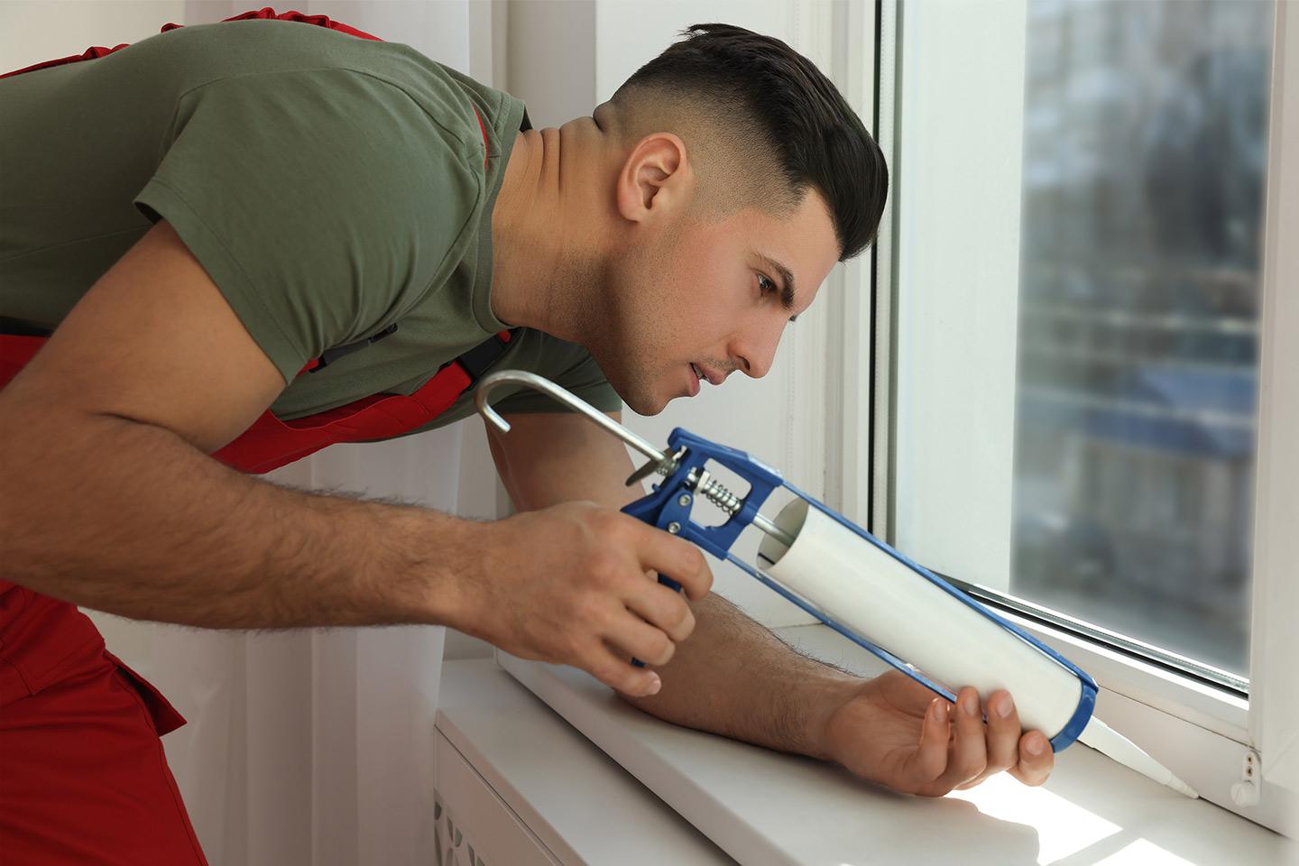 Man sealing window with caulking gun